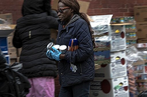 A volunteer carries canned food and a bag of carrots at St. Stephen Outreach in the Brooklyn borough of New York, on Friday, March 20, 2020. For decades, American nonprofits have relied on a cadre of volunteers who quite suddenly aren't able to show up. With millions staying home during the pandemic, charities that help the country's neediest are facing even greater need. Many Americans have now been ordered to shelter in place, but there is an exception for people providing essential services, and that includes food bank volunteering. (AP Photo/Wong Maye-E)