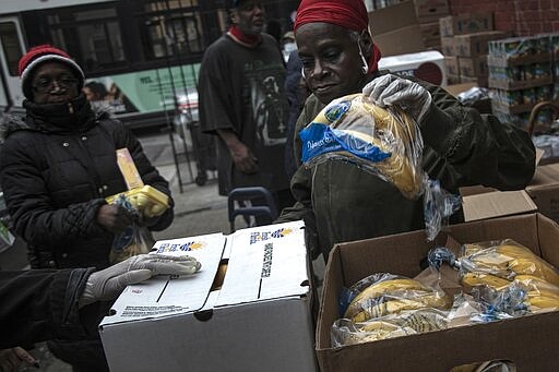 A volunteer gives out a bag of bananas at St. Stephen Outreach in the Brooklyn borough of New York, on Friday, March 20, 2020. For decades, American nonprofits have relied on a cadre of volunteers who quite suddenly aren't able to show up. With millions staying home during the pandemic, charities that help the country's neediest are facing even greater need. Many Americans have now been ordered to shelter in place, but there is an exception for people providing essential services, and that includes food bank volunteering. (AP Photo/Wong Maye-E)