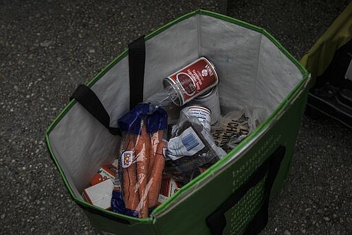 A bag of food donations is filled with canned food, carrots, chicken and juice at St. Stephen Outreach in the Brooklyn borough of New York, on Friday, March 20, 2020. For decades, American nonprofits have relied on a cadre of volunteers who quite suddenly aren't able to show up. With millions staying home during the pandemic, charities that help the country's neediest are facing even greater need. (AP Photo/Wong Maye-E)