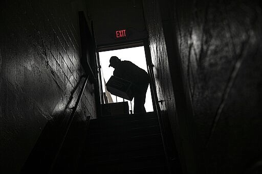 A volunteer is seen in silhouette as he carries cartons of food donations at St. Stephen Outreach in the Brooklyn borough of New York, on Friday, March 20, 2020. For decades, American nonprofits have relied on a cadre of volunteers who quite suddenly aren't able to show up. With millions staying home during the pandemic, charities that help the country's neediest are facing even greater need. Many Americans have now been ordered to shelter in place, but there is an exception for people providing essential services, and that includes food bank volunteering. (AP Photo/Wong Maye-E)