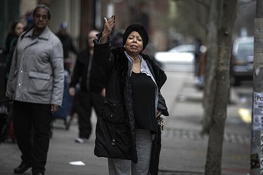 Sheila Williams who manages the soup kitchen and food pantry at St. Stephen Outreach, tells people waiting in line for their food donations to keep bigger distances between one another, in the Brooklyn borough of New York, on Friday, March 20, 2020. Williams usually has 25 volunteers to feed about 100 people a day at St. Stephen Outreach in Brooklyn. Now she's down to just 10 volunteers and says that there are more people waiting in line for food. (AP Photo/Wong Maye-E)