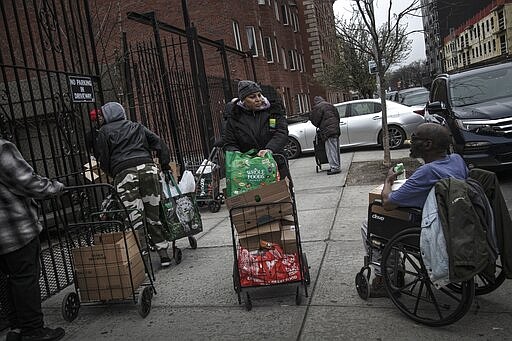 Elizabeth Pantojas 52, center, pushes her cart of food donations from St. Stephen Outreach in the Brooklyn borough of New York, on Friday, March 20, 2020. For decades, American nonprofits have relied on a cadre of volunteers who quite suddenly aren't able to show up. With millions staying home during the pandemic, charities that help the country's neediest are facing even greater need. Many Americans have now been ordered to shelter in place, but there is an exception for people providing essential services, and that includes food bank volunteering. (AP Photo/Wong Maye-E)