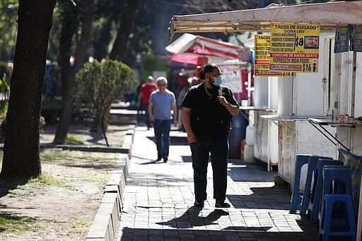 A man wearing a face mask walks past street stalls selling food, most of which were already open for business for the day, in Mexico City, Wednesday, March 25, 2020. While some businesses have shifted to work from home and more citizens are observing social distancing measures to slow the spread of the new coronavirus, many Mexicans who live day to day from what they can earn selling or scavenging in the streets say they do not have that economic luxury and must go on working as long as they can. (AP Photo/Rebecca Blackwell)