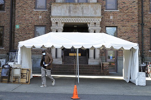 An employee wears a mask as he walks near an entrance to Western State Hospital, Thursday, March 19, 2020, in Lakewood, Wash. A patient and a worker at the facility, Washington state's largest psychiatric hospital, have tested positive for COVID-19. The tent shown behind him will eventually be used for screening employees for symptoms of the virus as they arrive for work. (AP Photo/Ted S. Warren)