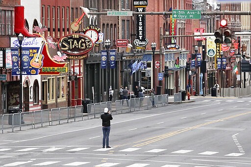 A man stands in the middle of Broadway to take a picture, where the streets and sidewalks are normally filled Monday, March 23, 2020, in Nashville, Tenn. More cities and counties in Tennessee have issued strict orders for nonessential businesses to shut down temporarily and people to stay at home as much as possible to curb the spread of the coronavirus. (AP Photo/Mark Humphrey)