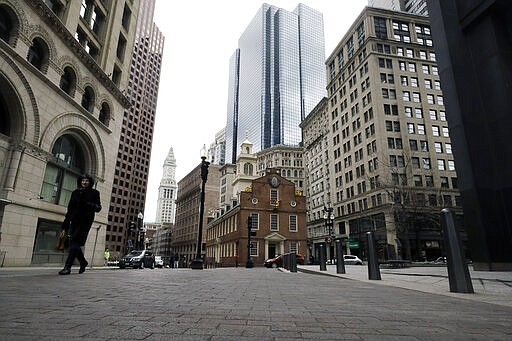 A passer-by walks a nearly empty sidewalk near the Old State House, center, in downtown Boston, Tuesday, March 24, 2020. Many people are working from home in the state, while many businesses have closed indefinitely out of concern about the spread of the coronavirus. (AP Photo/Steven Senne)