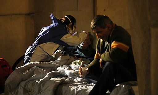 A volunteer nurse wearing a mask tends to an homeless in Milan, early Wednesday, March 25, 2020. The new coronavirus causes mild or moderate symptoms for most people, but for some, especially older adults and people with existing health problems, it can cause more severe illness or deaths. (AP Photo/Antonio Calanni)