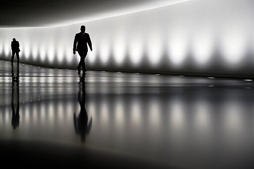 Two persons walk through a tunnel between the plenary hall and an office building of the German parliament Bundestag in Berlin, Germany, Wednesday, March 25, 2020. The parliament meet for a session to vote about new package of measures to cushion the devastating effects of the virus outbreak on the economy. In order to slow down the spread of the coronavirus, the German government has considerably restricted public life and asked the citizens to stay at home. The new coronavirus causes mild or moderate symptoms for most people, but for some, especially older adults and people with existing health problems, it can cause more severe illness or death. (AP Photo/Markus Schreiber)