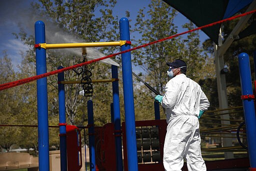 A worker cleans and disinfects playground equipment at a park to stop the spread to the coronavirus, Wednesday, March 25, 2020, in Las Vegas. (AP Photo/John Locher)