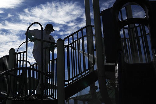 A worker cleans and disinfects playground equipment due to the coronavirus outbreak at a park Wednesday, March 25, 2020, in Las Vegas. (AP Photo/John Locher)