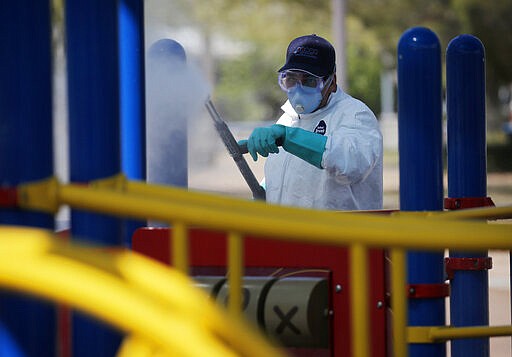 A worker cleans and disinfects playground equipment at a park to stop the spread to the coronavirus, Wednesday, March 25, 2020, in Las Vegas. (AP Photo/John Locher)