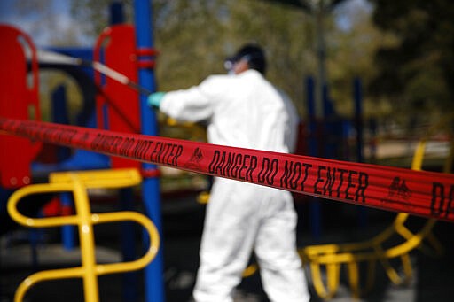 A worker cleans and disinfects playground equipment due to the coronavirus at a park Wednesday, March 25, 2020, in Las Vegas. (AP Photo/John Locher)