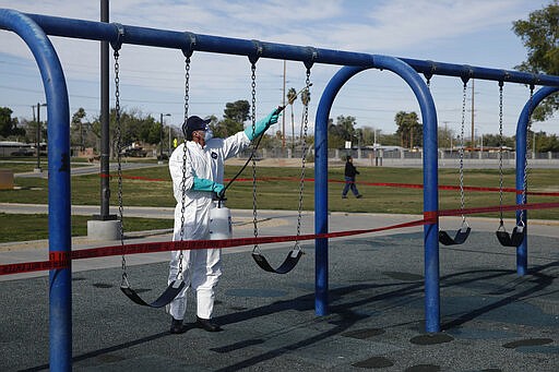 A worker cleans and disinfects playground equipment due to the coronavirus outbreak at a park Wednesday, March 25, 2020, in Las Vegas. (AP Photo/John Locher)