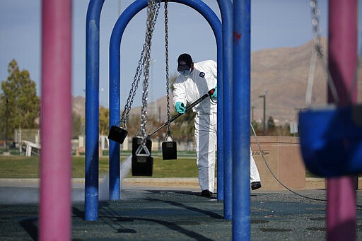 A worker cleans and disinfects playground equipment due to the coronavirus outbreak at a park Wednesday, March 25, 2020, in Las Vegas. (AP Photo/John Locher)