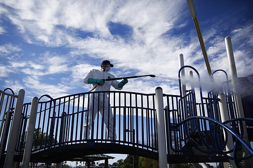 A worker cleans and disinfects playground equipment due to the coronavirus outbreak at a park Wednesday, March 25, 2020, in Las Vegas. (AP Photo/John Locher)