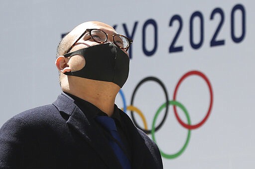 A man walks in front of a Tokyo Olympics logo at the Tokyo metropolitan government headquarters building in Tokyo, Wednesday, March 25, 2020. The Olympic torch relay was postponed Tuesday because the Tokyo Games themselves were pushed back to 2021. (AP Photo/Koji Sasahara)