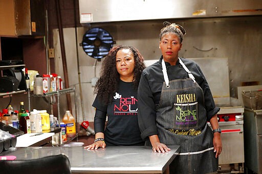 In this March 24, 2020, photo, Keisha Henry, right, and her business partner Erica Norwood pose for a portrait inside their lounge and catering business in New Orleans. Henry said she lost about $10,000 in revenue last week after three big functions she was slated to cater ended up canceling. Meanwhile, she still has expenses related to launching a bar and lounge six months ago. Henry said she regrettably had to lay off several employees. (AP Photo/Gerald Herbert)