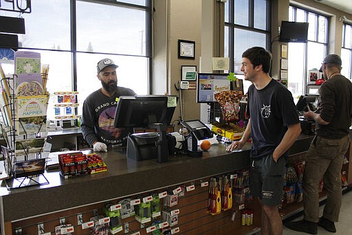 In this photo taken March 20, 2020, Mike Johnston, a clerk at the Maupin Market in tiny Maupin, Oregon, helps a customer while wearing a latex glove to protect himself from the new coronavirus. Tiny towns tucked into Oregon's windswept plains and cattle ranches miles from anywhere in South Dakota might not have had a single case of the new coronavirus yet, but their residents fear the spread of the disease to areas with scarce medical resources, the social isolation that comes when the only diner in town closes its doors and the economic free fall that's already hitting them hard. (AP Photo/Gillian Flaccus)