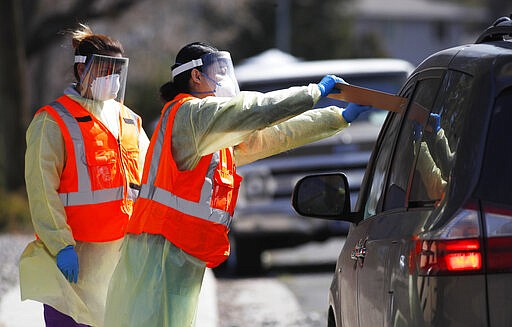 Medical technicians slide a clipboard with paperwork through the window of a van to a motorist coming in for a test for the new coronavirus Wednesday, March 25, 2020, at a drive-thru site at Stride Community Health Aurora, Colo. The new coronavirus causes mild or moderate symptoms for most people, but for some, especially older adults and people with existing health problems, it can cause more severe illness or death. (AP Photo/David Zalubowski)