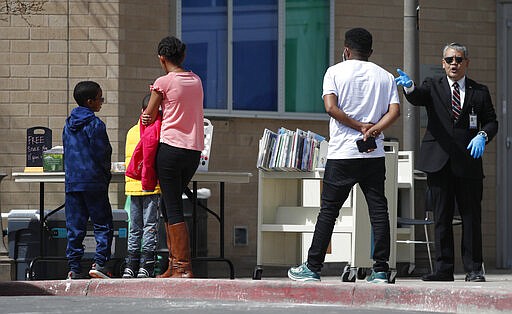 Phillip Challis, right, branch manager of the Central Library in Aurora, Colo., directs a family to free lunches and books outside the facility in an effort to help residents during the spread of the new coronavirus Wednesday, March 25, 2020, in Aurora, Colo. The lunches are offered weekdays from noon to 1 p.m. outside the library. The new coronavirus causes mild or moderate symptoms for most people, but for some, especially older adults and people with existing health problems, it can cause more severe illness or death. (AP Photo/David Zalubowski)