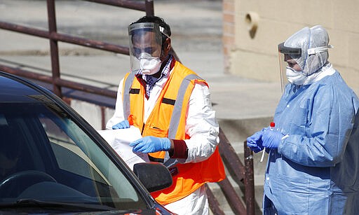 As a medical worker checks paperwork, left, a technician waits with a kit to administer a test for the new coronavirus Wednesday, March 25, 2020, at a drive-thru testing site at Stride Community Health in Aurora, Colo. The new coronavirus causes mild or moderate symptoms for most people, but for some, especially older adults and people with existing health problems, it can cause more severe illness or death. (AP Photo/David Zalubowski)