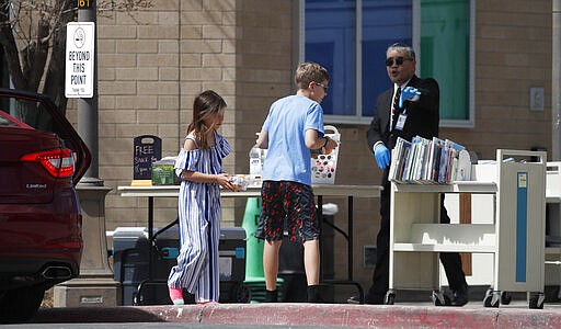 Phillip Challis, right, branch manager of the central library for the City of Aurora, Colo., offers free books and lunches to city resients under the age of 18 in an effort to reach out during the spread of the new coronavirus Wednesday, March 25, 2020, in Aurora, Colo. The lunches are served from noon to 1 p.m. on weekdays. The new coronavirus causes mild or moderate symptoms for most people, but for some, especially older adults and people with existing health problems, it can cause more severe illness or death. (AP Photo/David Zalubowski)