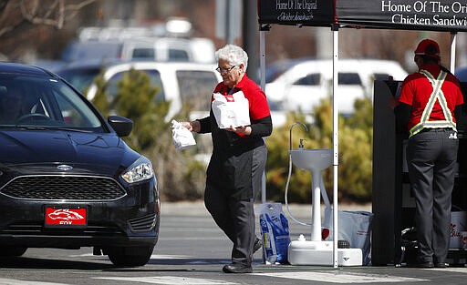 A worker carries bags of food to a motorist in a drive-thru line at fast food restaurant to reduce the spread of the new coronavirus Wednesday, March 25, 2020, in Aurora, Colo. The new coronavirus causes mild or moderate symptoms for most people, but for some, especially older adults and people with existing health problems, it can cause more severe illness or death. (AP Photo/David Zalubowski)