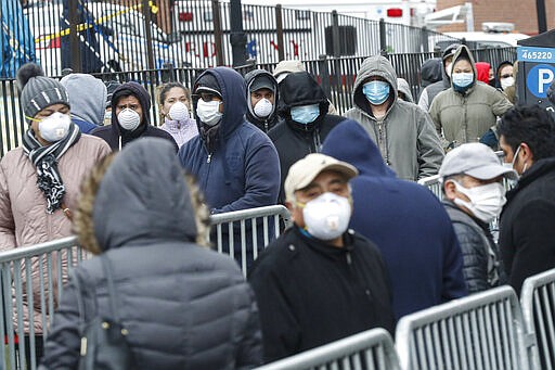 Patients wear personal protective equipment while maintaining social distancing as they wait in line for a COVID-19 test at Elmhurst Hospital Center, Wednesday, March 25, 2020, in New York. Gov. Andrew Cuomo sounded his most dire warning yet about the coronavirus pandemic Tuesday, saying the infection rate in New York is accelerating and the state could be as close as two weeks away from a crisis that sees 40,000 people in intensive care. Such a surge would overwhelm hospitals, which now have just 3,000 intensive care unit beds statewide. (AP Photo/John Minchillo)