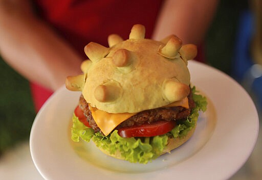 Restaurant owner Hoang Tung holds up a &quot;Corona burger&quot; in Hanoi, Vietnam on Wednesday, March 25, 2020. As the world is fighting against the Covid-19 pandemic, the Vietnamese restaurant hopes to cheer people up with their new creation, in which the burger buns shape like a coronavirus. The new coronavirus causes mild or moderate symptoms for most people, but for some, especially older adults and people with existing health problems, it can cause more severe illness or death. (AP Photo/Hau Dinh)