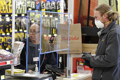 Hardware store clerk Marilyn Larson, left, works behind a plexiglass barrier built a few days earlier by a co-worker to help protect employees and customers during the coronavirus outbreak as customer Phill Kuypers checks-out Wednesday, March 25, 2020, in Seattle. Kuypers wore a mask to take extra precautions while in public because his wife is pregnant. (AP Photo/Elaine Thompson)