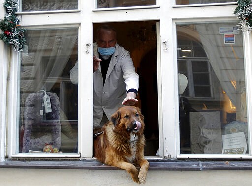 A man pets a dog that sits in a window downtown Prague, Czech Republic, Tuesday, March 24, 2020. The Czech government extended Monday its strict restrictions on movement and other activities until at least April 1, in efforts to contain the outbreak of the new coronavirus. (AP Photo/Petr David Josek)