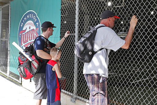 FILE - In this March 12, 2020, file photo, baseball fans look through a fence at Hammond Stadium after a game between the Minnesota Twins and the Baltimore Orioles was canceled, in Fort Myers, Fla. On MLB&#146;s opening day, ballparks will be empty with the start of the season on hold because of the coronavirus pandemic.  (AP Photo/Elise Amendola, File)