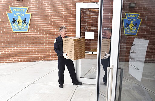 Scranton city police officer Dave Rose carries boxes of pizzas from Buona Pizza to the Scranton Police Department headquarters in Scranton, Pa. Tuesday, March 24, 2020. Fidelity Bank purchased the 40 pizzas for hospital workers and the police department to thank them for their work during the COVID-19 pandemic.  (Sean McKeag /The Times Tribune via AP)