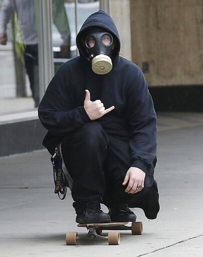 A skateboarder makes the Hang Loose sign as he rolls a sidewalk in Wilkes-Barre Pa., Tuesday, March 24, 2020 while wearing a gas mask. (Dave Scherbenco/The Citizens' Voice via AP)