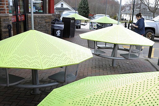 A woman walks to the entrance of a convenience store through a section of outdoor seating that has had the protective umbrellas lowered over the seats to prevent people from gathering there, in order to promote social distancing due to caronavirus Wednesday, March 25, 2020, in New Castle, Pa. (AP Photo/Keith Srakocic)