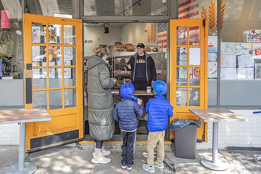 Molly Carroll, center, an employee of the Baker Street Bread Co. in Philadelphia, gets the bread order ready for a family Tuesday March 24, 2020. The store will not allow foot traffic inside the store because of the coronavirus so they created a curbside system that allows customers to walk up and receive orders. (Michael Bryant/The Philadelphia Inquirer via AP)