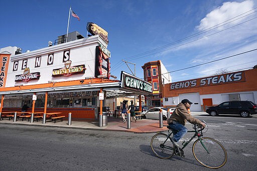 A cyclist passes by a less busy Geno's Steaks in Philadelphia on Tuesday, March 24, 2020. Non-essential businesses are closed and a stay-at-home order has been issued by the city, with exceptions to allow people to purchase essential goods and food or seek medical attention, to try to reduce the spread of the coronavirus. Outdoor activities such as walking, running and cycling are permitted under the order. (Jessica Griffin/The Philadelphia Inquirer via AP)