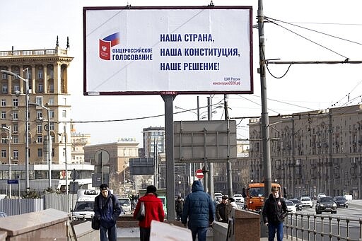 People walk past a billboard that reads: &quot;Our country, Our Constitution, Our Decision&quot;, in a street in Moscow, Russia, Wednesday, March 25, 2020. Russian President Vladimir Putin has postponed a nationwide vote on proposed constitutional amendments that include a change potentially allowing him to stay in office until 2036. Putin cited the coronavirus in announcing the postponement of the vote that was originally scheduled for April 22. (AP Photo/Alexander Zemlianichenko)