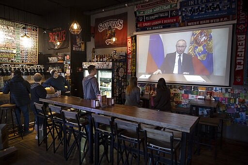 A few visitors and staff of the pub watching the broadcast of Russian President Vladimir Putin addresses Russian citizens on the State Television channels in Moscow, Russia, Wednesday, March 25, 2020. Putin has postponed a nationwide vote on proposed constitutional amendments that include a change that would allow him to seek another term in power. He also announced during a televised address to the nation that the government doesn't want Russians except those working in essential sectors to come to work next week. He said that stores, pharmacies and banks will stay open. (AP Photo/Alexander Zemlianichenko)