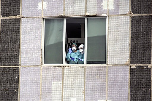 FILE, in this Wednesday, March 18, 2020 file photo, medical workers wearing face masks gesture from hospital La Paz in Madrid, Spain. The coronavirus is winning a war of attrition waged against health care workers throughout the world but more so in Spain, where necessary equipment to shield them from contagion and enough testing kits for the new virus have been lacking for weeks. The new coronavirus causes mild or moderate symptoms for most people, but for some, especially older adults and people with existing health problems, it can cause more severe illness or death. (AP Photo/Manu Fernandez, File)