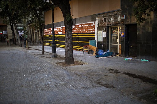 In this Thursday, March 19, 2020 photo, a man from sub-Saharan Africa sleeps in an empty street in downtown Barcelona, Spain. Authorities are scrambling to get as many homeless people off the streets without cramming them into a group shelter, where the risk of getting infected with the virus could be even greater.(AP Photo/Emilio Morenatti)