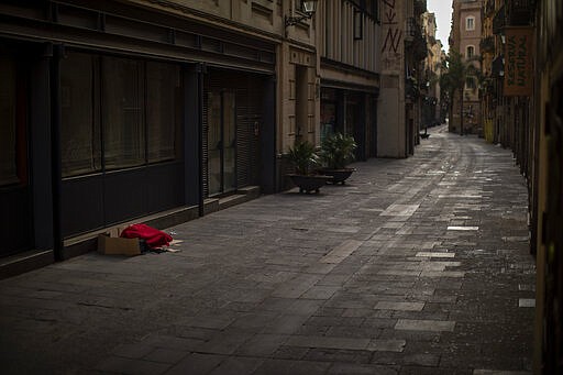 In this Sunday, March 22, 2020 photo, a man covered with a blanket sleeps in an empty street in Barcelona, Spain. In Barcelona sleeping figures with boxes and blankets punctuate the mostly empty city. They are Barcelona's homeless, and there are about 1,000 of them. (AP Photo/Emilio Morenatti)