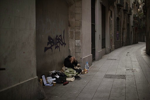 In this Saturday, March 21, 2020 photo, Javier Redondo, 40, covers his head with his hands as he waits for alms on an empty street in Barcelona, Spain. While authorities are telling people to stay at home amid the COVID-19 outbreak, others as Javier are having to stay on the street -- because they have no choice. &quot;I am not afraid of the virus because my physical condition is very good. If I caught the virus, my body would expel it as if it were a gastroenteritis&quot;, Javier said. (AP Photo/Emilio Morenatti)