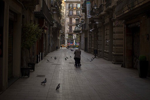 In this Saturday, March 21, 2020 photo, a woman pushes a cart with her belongings as she walks along an empty street in downtown Barcelona, Spain. While Spanish authorities tell the public that staying home is the best way to beat the coronavirus pandemic, some people are staying out because home has come to mean the streets of Madrid and Barcelona. (AP Photo/Emilio Morenatti)