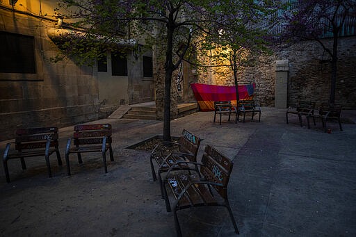 In this Saturday, March 21, 2020 photo, a blanket is used as a shelter in the corner of a square in downtown Barcelona, Spain. With Spain one of the world's worst-hit countries by the new coronavirus, and the government ordering a national lockdown, the country's streets are largely deserted. (AP Photo/Emilio Morenatti)