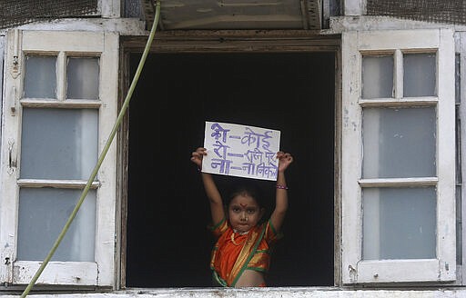 A girl dressed in traditional attire to celebrate &quot;Gudi Padwa&quot;, or the Marathi New Year, stands by a window and holds a placard with an acronym for the Coronavirus that reads in hindi &quot;Nobody should come out on the roads,&quot; in Mumbai, India, Wednesday, March 25, 2020. The world's largest democracy went under the world's biggest lockdown Wednesday, with India's 1.3 billion people ordered to stay home in a bid to stop the coronavirus pandemic from spreading and overwhelming its fragile health care system as it has done elsewhere. For most people, the new coronavirus causes mild or moderate symptoms, such as fever and cough that clear up in two to three weeks. For some, especially older adults and people with existing health problems, it can cause more severe illness, including pneumonia and death. (AP Photo/Rafiq Maqbool)