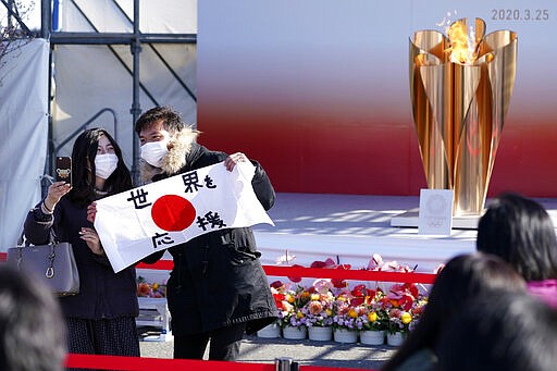 Visitors pose with a national flag with characters reading &quot;Supporting the world&quot; near the Olympic Flame during the Olympic &quot;Flame of Recovery&quot; display ceremony in Iwaki, Fukushima Prefecture, northern Japan, Wednesday, March 25, 2020. IOC President Thomas Bach has agreed &quot;100%&quot; to a proposal of postponing the Tokyo Olympics for about one year until 2021 because of the coronavirus outbreak. (AP Photo/Eugene Hoshiko)