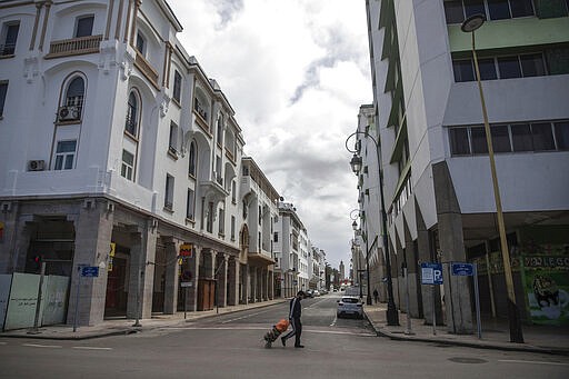 A man walks home with groceries in an empty street following the announcement of a health state of emergency and home confinement orders, in Rabat, Morocco, Sunday, March 22, 2020.  For some people the COVID-19 coronavirus causes mild or moderate symptoms, but for some it can cause severe illness including pneumonia.(AP Photo/Mosa'ab Elshamy)