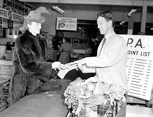 FILE - In this Feb. 14, 1943 file photo Mrs. Caven holds her new point ration book as the grocer indicates the proper stamps to cover purchases in New York. Each person had 48 points for use during March. Not since World War II, when people carried Ration Books with stamps that allowed them to purchase meat, sugar, butter, cooking oil and gasoline, has the entire nation been asked to truly sacrifice for a greater good. (AP Photo/Carl Nesensohn, File)