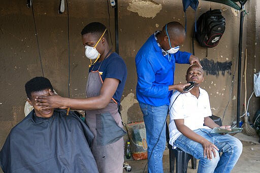 Barbers wearing protective masks attend to customers in the township of Soweto, outside Johannesburg, South Africa, Wednesday March 25, 2020. South Africa will go into a nationwide lockdown for 21 days starting Friday morning, in an effort to mitigate the spread to the coronavirus. The new coronavirus causes mild or moderate symptoms for most people, but for some, especially older adults and people with existing health problems, it can cause more severe illness or death.(AP Photo/Jerome Delay)